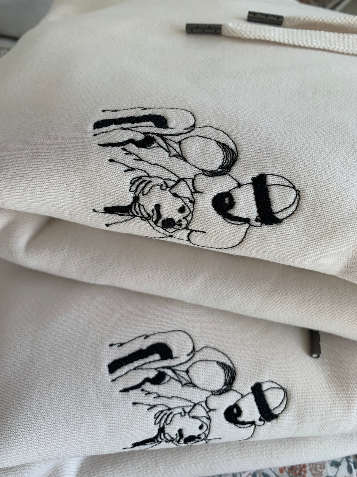 Close-up hoodies  with black embroidered line-art illustrations of a couple photo.