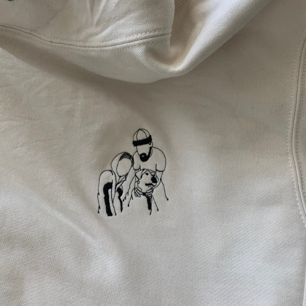 Close-up of an off-white hoodie, pockets with a black line-art graphic on the chest from a couple photo.