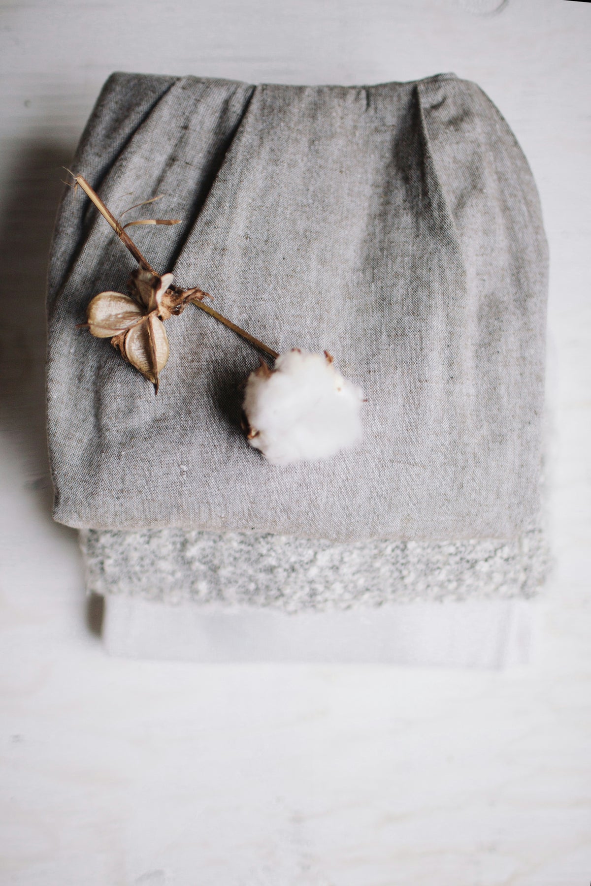 Gray natural and organic fabric with a cotton flower and dried plant on a light background