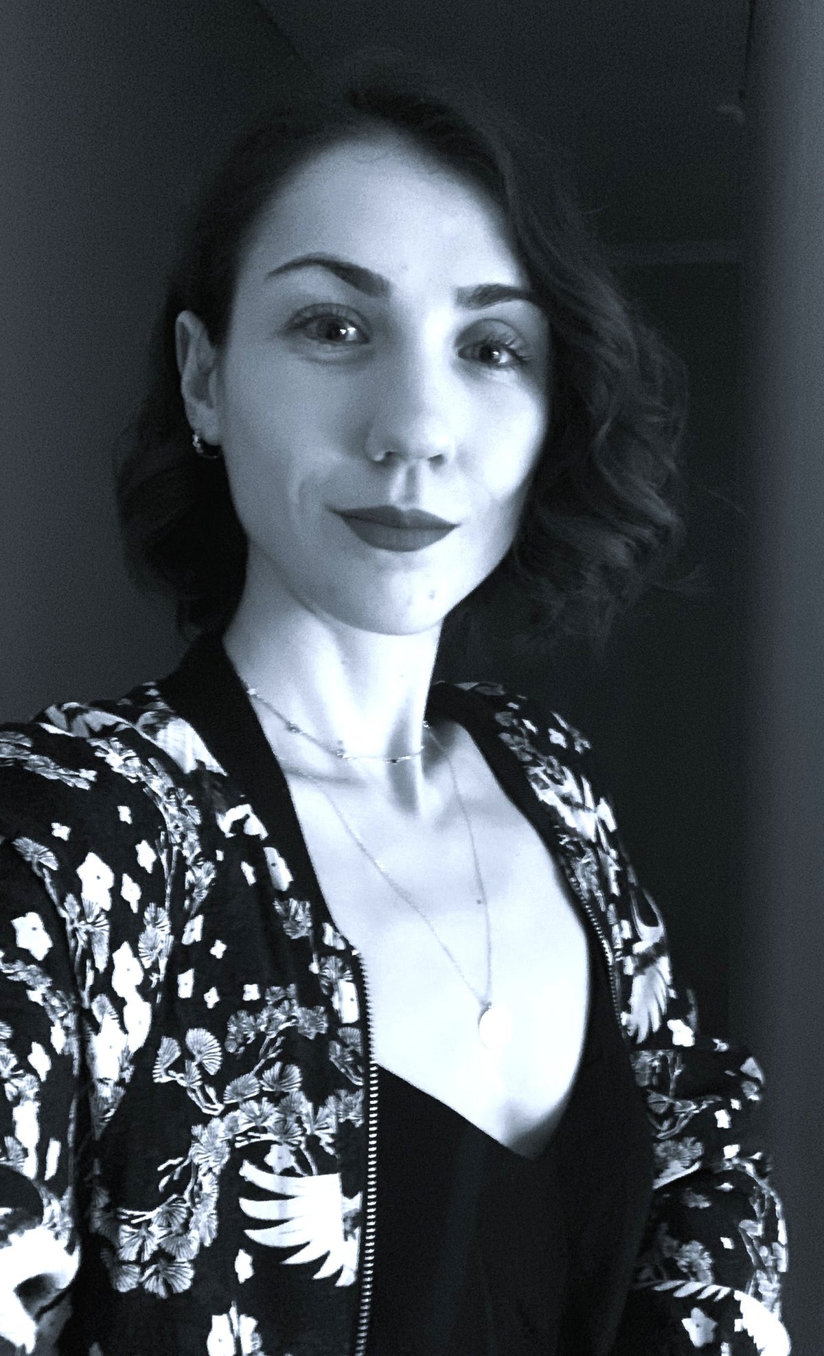 Miilo team member - A black and white portrait of a woman wearing a black and white patterned bomber jacket over a black top.