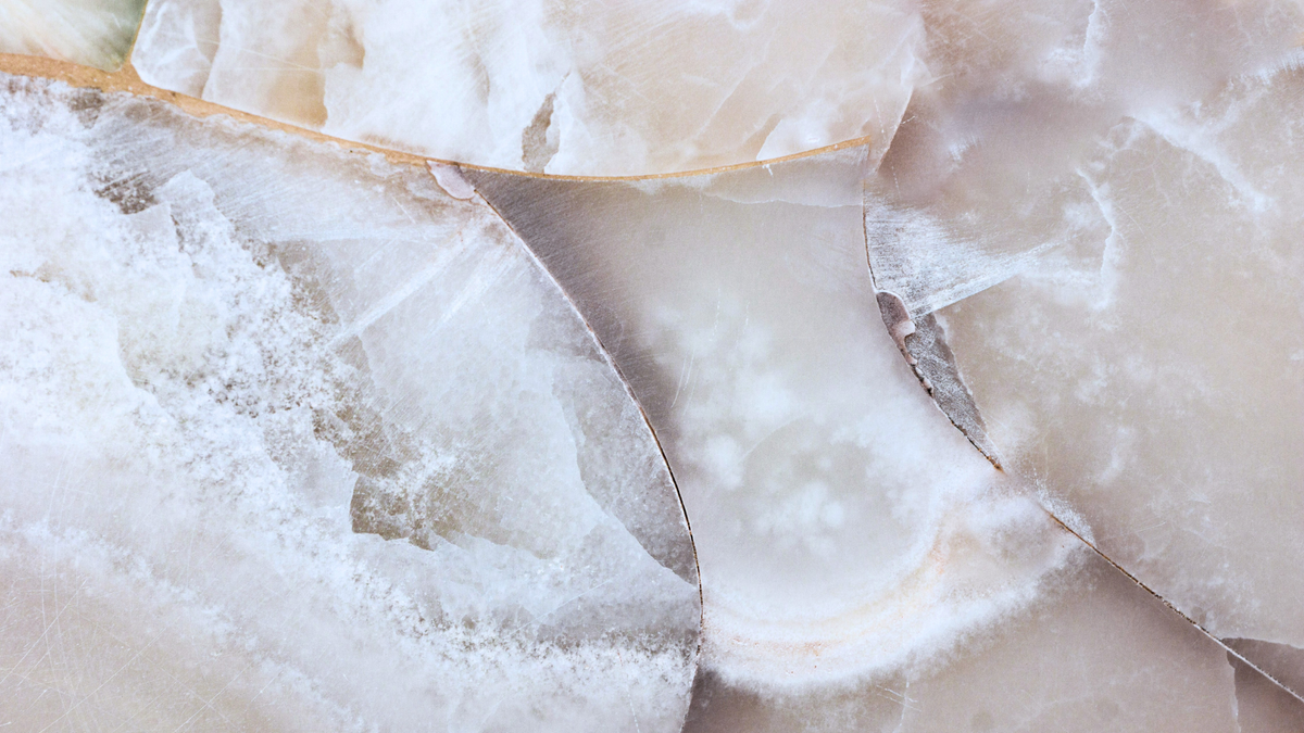 A close-up of polished agate or marble-like stone slices with swirling white, cream, beige, and soft gray veining.