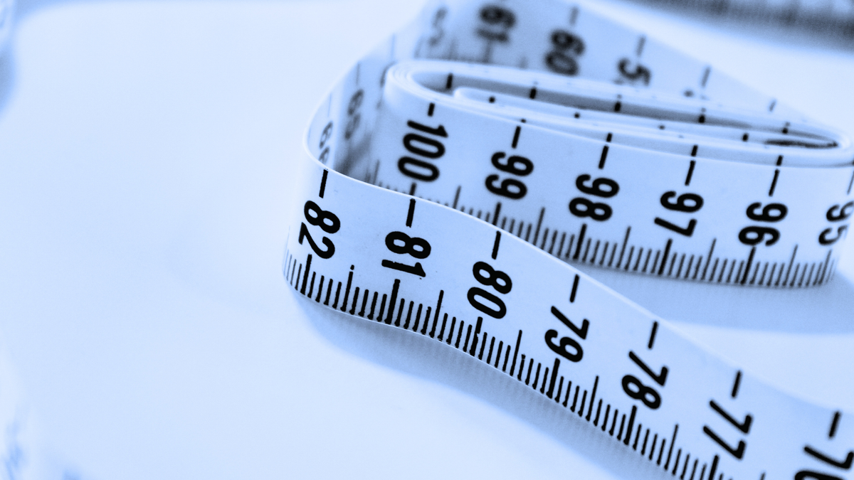 A close-up of a white measuring tape with black printed numbers and markings, coiled on a light blue surface.